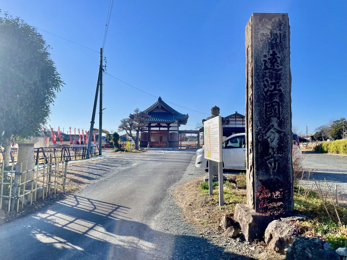 特別史跡・遠江国分寺跡の入口。手前に「特別史跡 遠江國分寺址」と刻まれた石碑が立ち、奥に堂と説明板が見える。青空の広がる冬の日の風景。